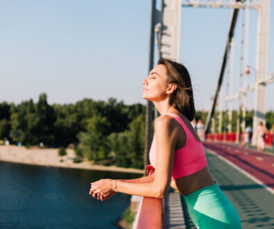 Sporty woman in fitting sport wear at sunset at modern bridge with river view look around enjoying summer weather