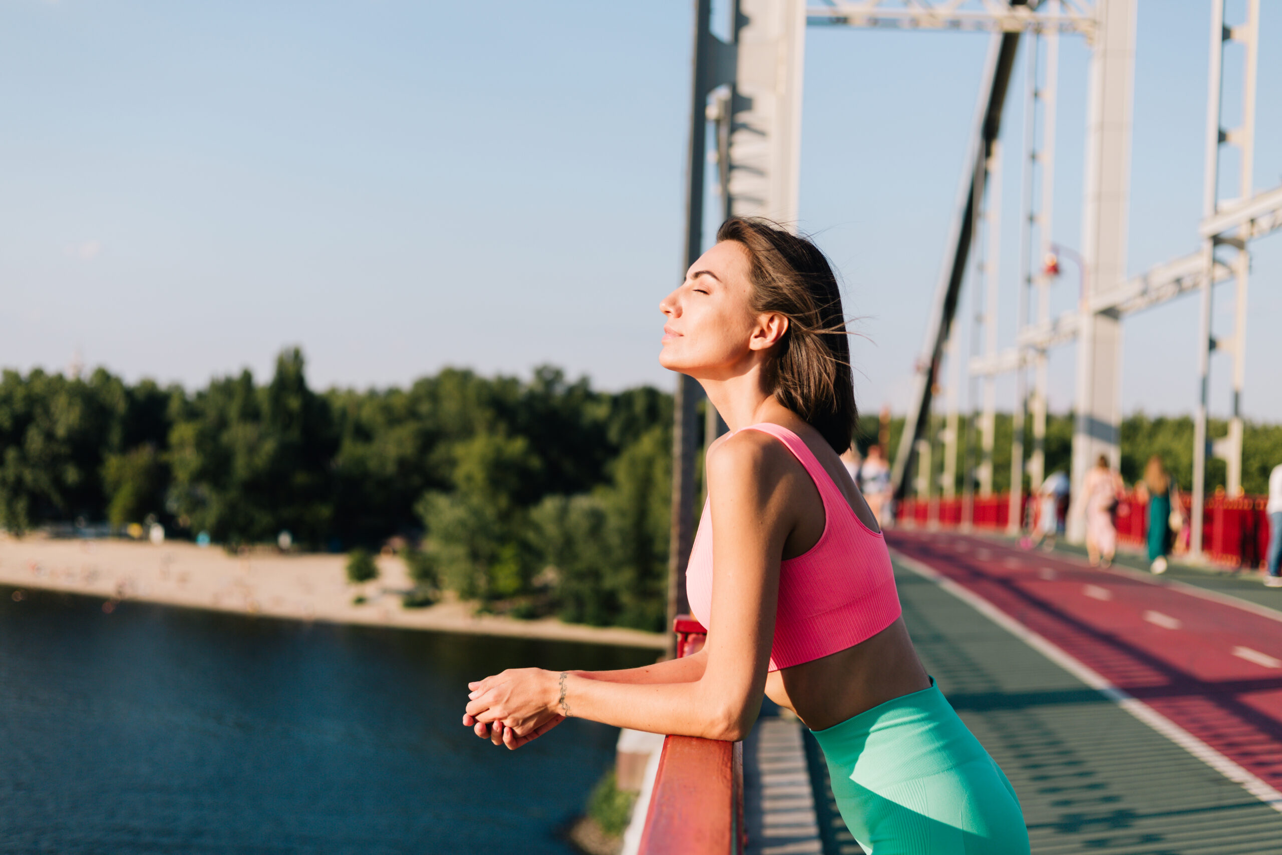 Sporty woman in fitting sport wear at sunset at modern bridge with river view look around  enjoying summer weather