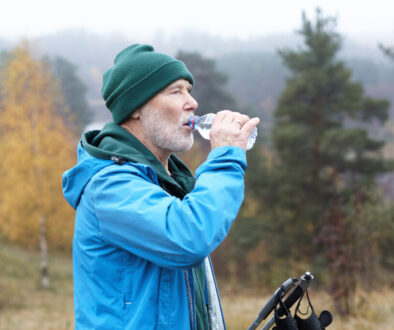 Sports, active lifestyle and refreshment concept. Autumn portrait of handsome sporty male pensioner with thick white beard refreshing himself after nordic walking, drinking water from plastic bottle