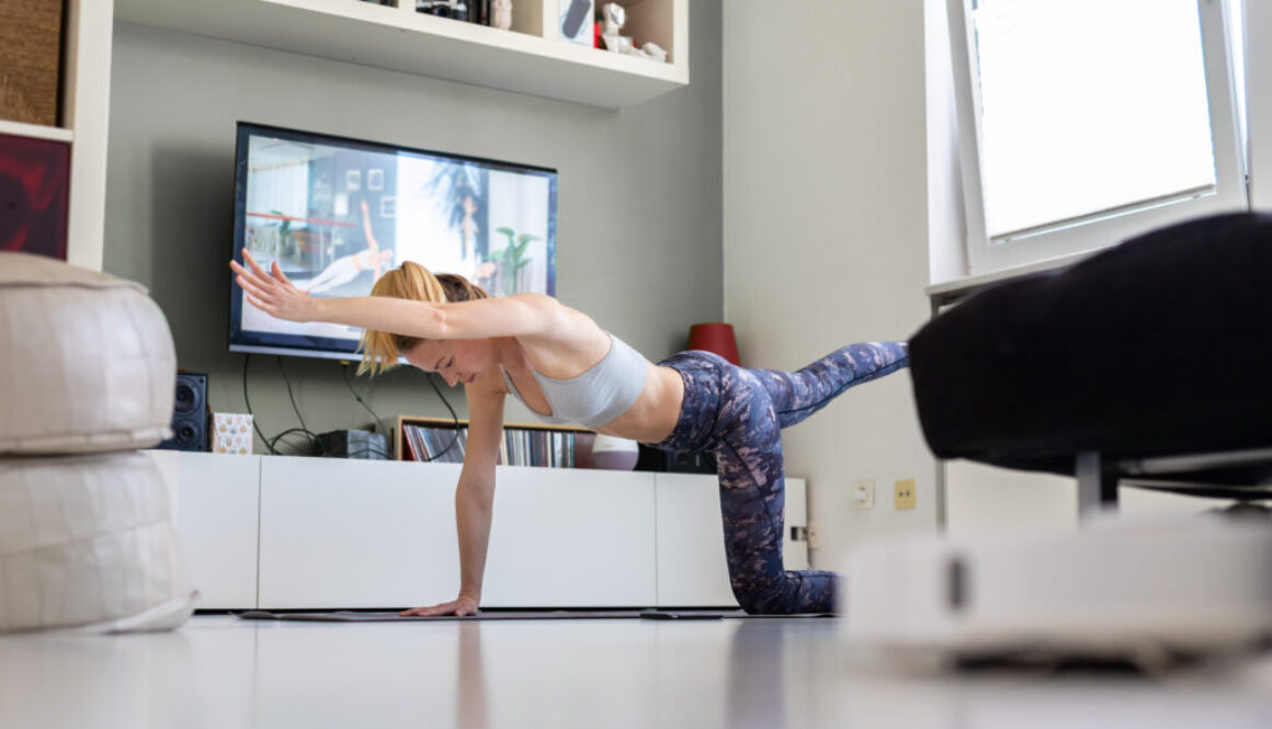 Attractive sporty woman working out at home, doing pilates exercise in front of television in her living room. Social distancing. Stay healthy and stay at home during corona virus pandemic