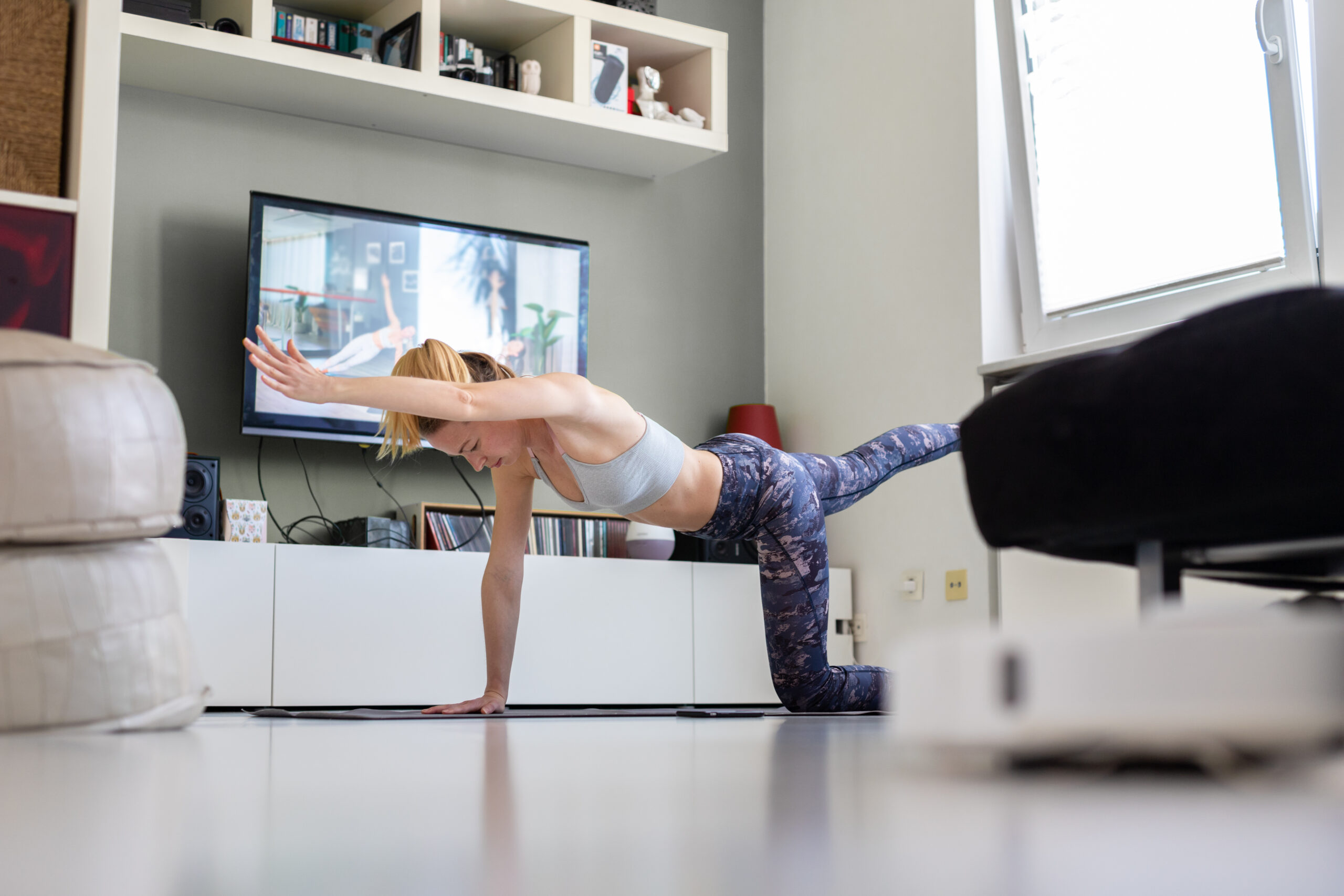 Attractive sporty woman working out at home, doing pilates exercise in front of television in her living room. Social distancing. Stay healthy and stay at home during corona virus pandemic