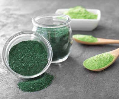 Spirulina and wheat grass powder in kitchenware on grey background