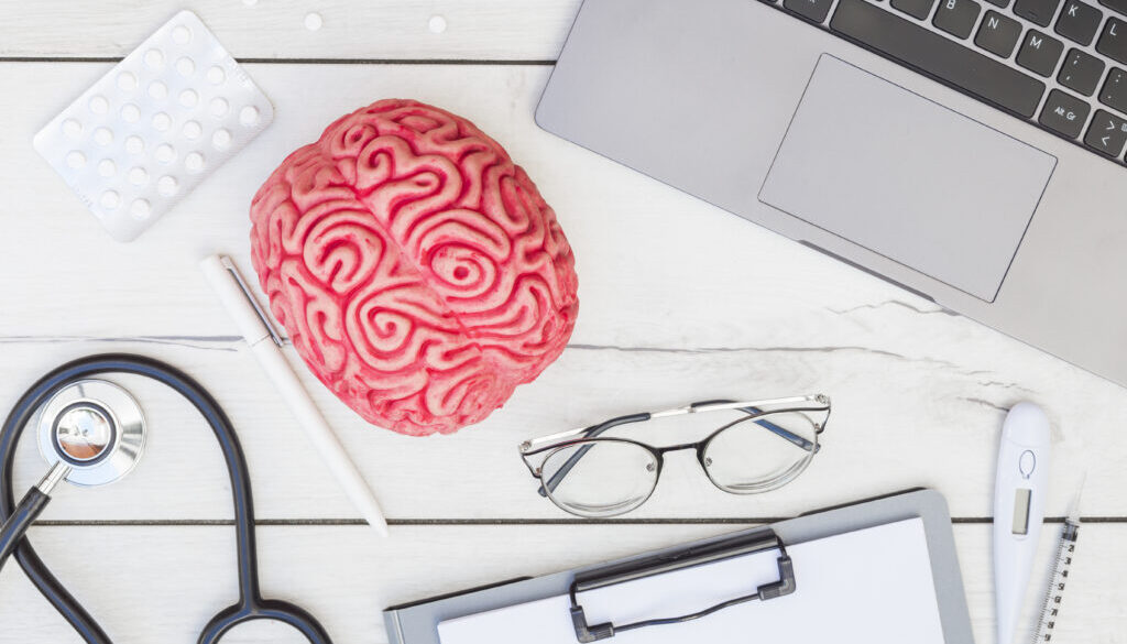 pink-brain-model-pills-stethoscope-pen-eyeglasses-clipboard-thermometer-syringe-laptop-wooden-desk