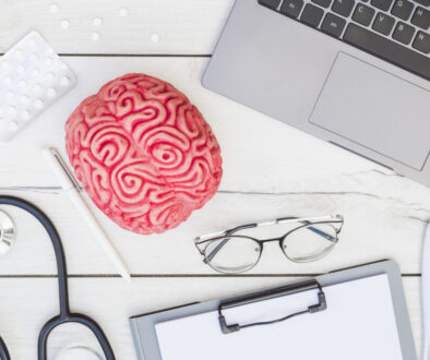 pink-brain-model-pills-stethoscope-pen-eyeglasses-clipboard-thermometer-syringe-laptop-wooden-desk